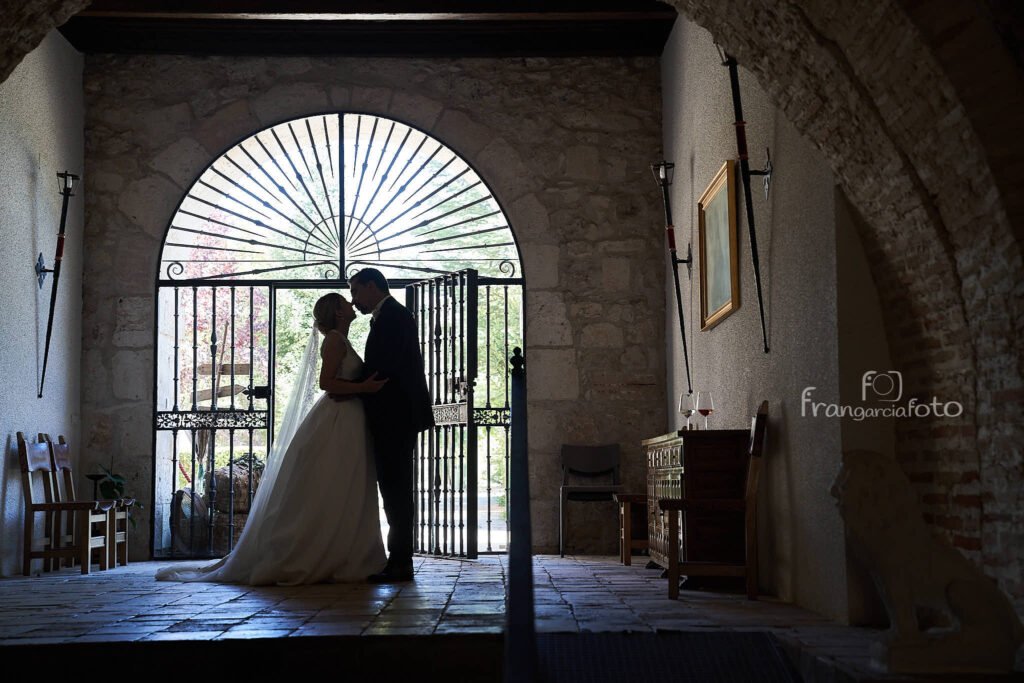 Pareja de novios besandose debajo de una puerta enrejada con forma de arco románico